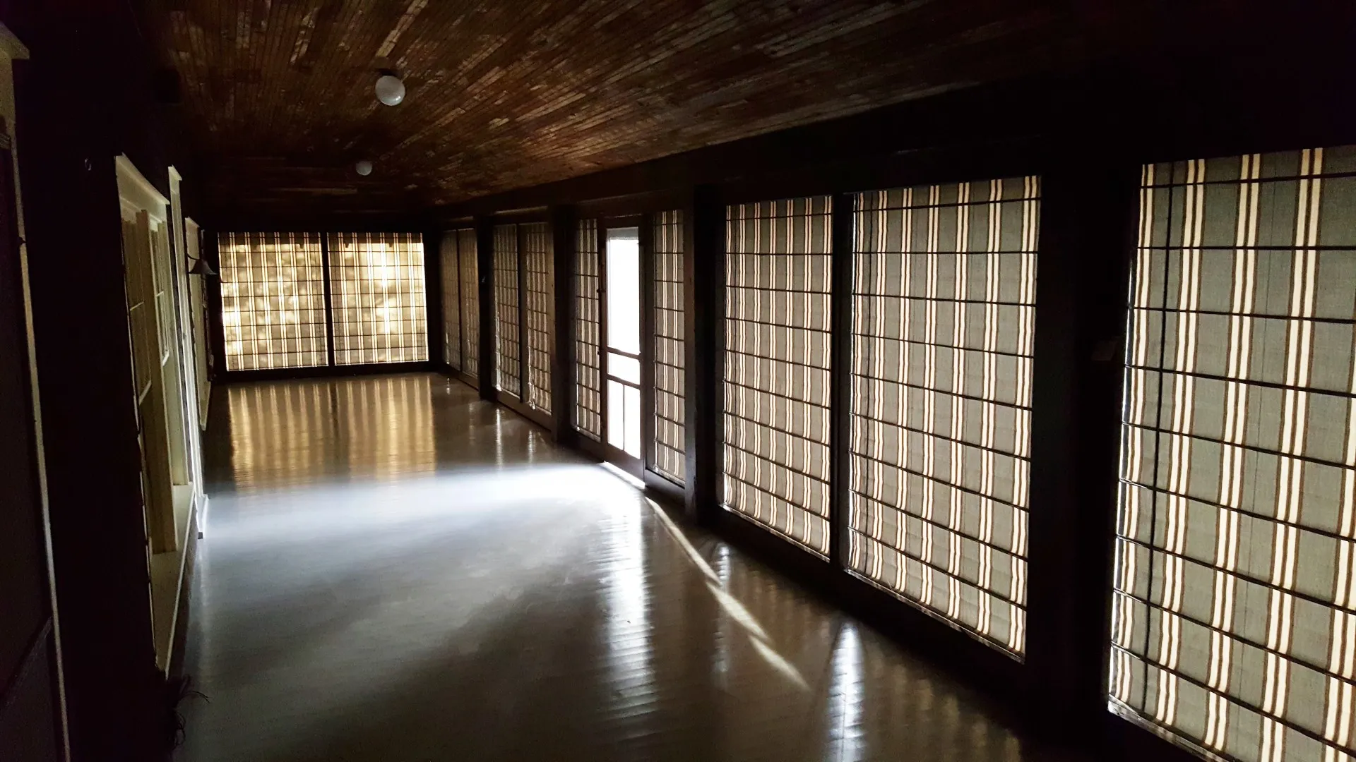 On Madeline Island the soft stripes give stained glass feel to porch,4768 Preston Stone (6) A long, narrow corridor with dark wooden ceiling and floor, lit by natural light through shoji-style paper screen windows on one side, evokes the tranquil ambiance of a shaded porch.